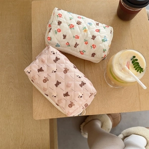 Detailed top view of quilted floral and bear pattern fabric makeup pouches on a wooden table