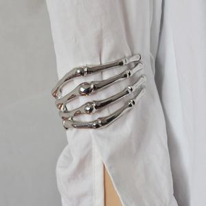 Macro shot of a silver skeleton hand arm cuff worn over a white shirt sleeve