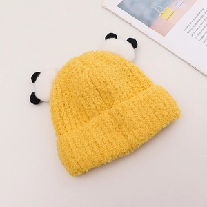 Dettaglio cappello neonato giallo a maglia con pompon a panda su sfondo decorativo