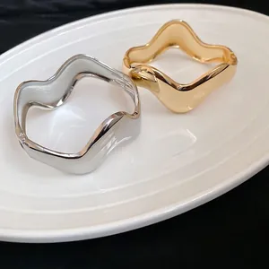 Minimalist irregular wave-shaped open bangles in polished gold and silver metal finishes