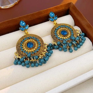 Dettaglio di orecchini vintage dorati con strass blu e nappe di perline in una scatola