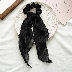 Detail of a black textured fabric hair scrunchie with long ribbons on a ceramic plate
