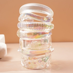 Chunky iridescent acrylic bangles stacked with textured geometric designs on soft pink backdrop
