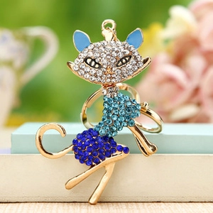 Detail of a gold cat keychain with blue rhinestones placed on a book against green foliage