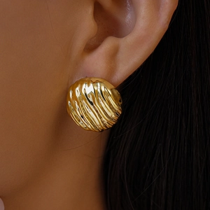 Gros plan de boucles d'oreilles créoles dorées aux motifs ondulés irréguliers élégants