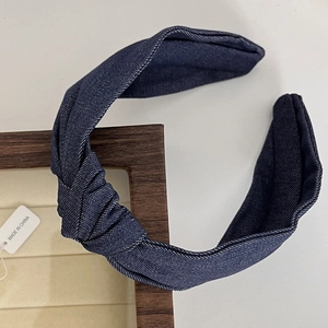 Close-up of deep blue denim knotted headband on a wooden display tray with white background