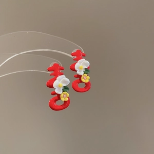 Macro shot of red Xi-character earrings with enamel floral details on a clear display stand
