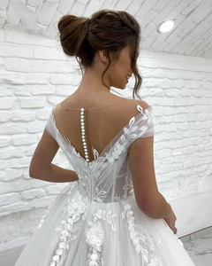 Detail of white bridal gown featuring pearl buttons on an open back with lace appliques