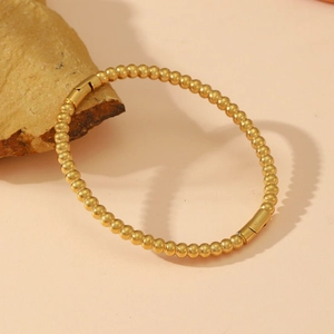 Polished gold beaded bracelet with clasp displayed on a textured natural rock pedestal