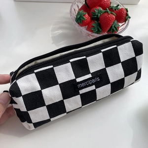 Detail of checkered canvas pencil case with merciparis label on a white desk