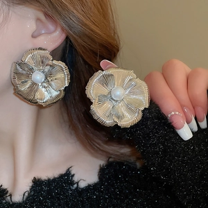 Macro shot of large metal flower earrings with white pearls on a model wearing ear studs