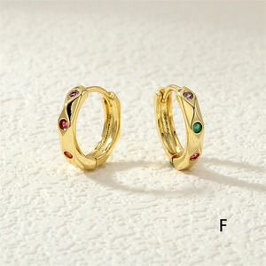 Macro view of gold hoop earrings with colorful zircon stones on textured background