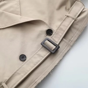 Détail du trench-coat kaki avec boutons noirs, boucle carrée et bords à franges