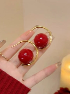 Detailed close-up of large glossy red pearl beads on gold-finish hoop earrings for women