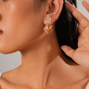 Macro shot of a gold bow earring with rhinestones and a brown leopard print pompom