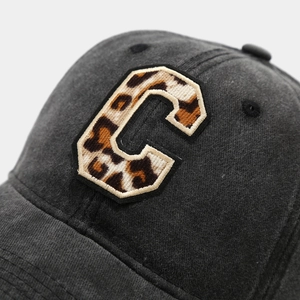 Macro detail of leopard print C patch embroidery on washed black denim baseball cap