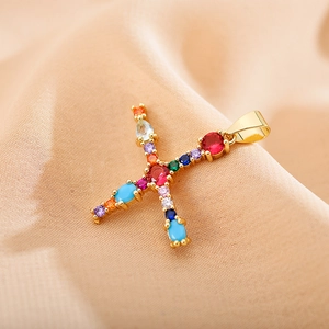 Close-up of golden letter X pendant with colorful cubic zirconia on beige fabric