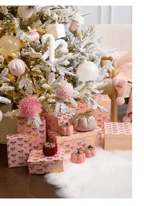Pink Christmas gift boxes with gold bows and velvet pumpkins under a snowy tree