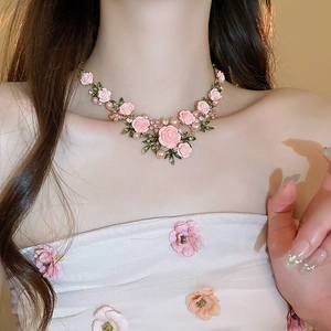 Detail of pink rose necklace with green leaves, pearls, and crystals on a model