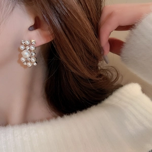 Detailed view of rectangle earrings featuring white pearls and clear crystals on gold base