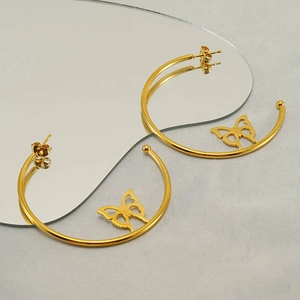 Detail of gold hoop earrings with butterfly charms on a creative mirrored background