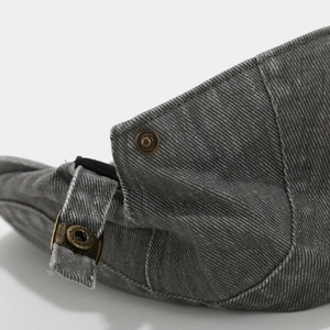 Detail of adjustable bronze buckle and washed denim texture on a vintage beret cap