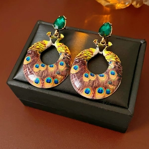 Close-up of vintage enamel peacock earrings with emerald drop gemstone on black box