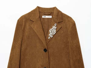 Dettaglio di un cappotto scamosciato marrone con spilla di strass scintillanti sul risvolto