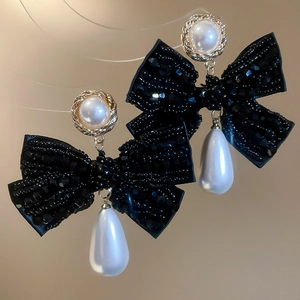 Close-up of bow earrings with crystal drops and large teardrop pearls on a warm background