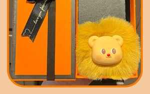 Close-up of a plush cream bear charm nestled in a premium orange gift box