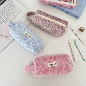 Three plush leopard print makeup pouches in pink, blue, and purple on a white desk