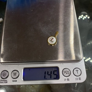 Detailed view of round natural shell alphabet letter L pendant weighing 1.45g on a scale