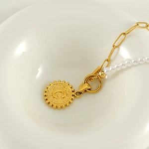 Detail of a pearl and gold clip chain necklace with a C letter coin pendant in a bowl