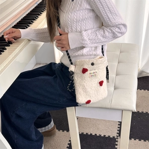 Detail of white plush crossbody bag with red hearts and textured woven shoulder strap