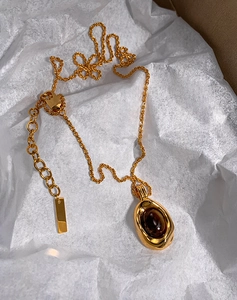 Detail of gold-plated tiger eye necklace with twisted chain on white silk paper