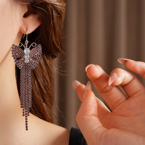 Primo piano di orecchini a farfalla in zircone viola con lunghe nappe di strass indossati