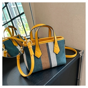 Detail of a yellow leather trim on a striped woven tote bag with detachable strap