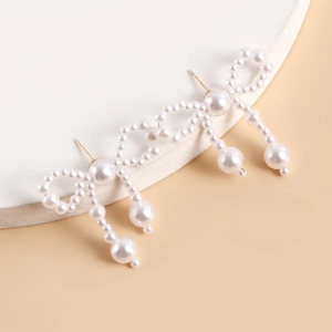 Detailed close-up of handmade faux pearl bow earrings with golden metal studs