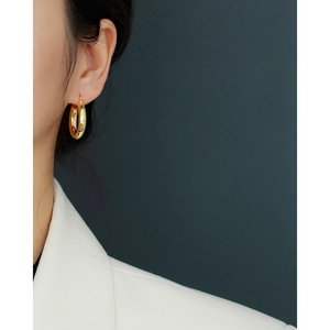Close-up of polished gold hoop earrings worn on ear with professional white blazer