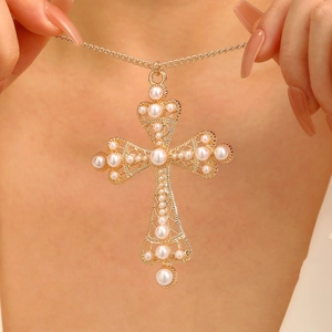 Detail shot of golden hollow cross pendant with multiple white pearls on a layered necklace