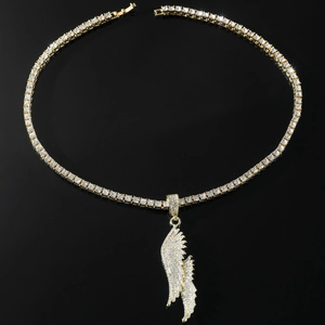 Detailed macro shot of golden iced out wing pendant with sparkling tennis chain on black background