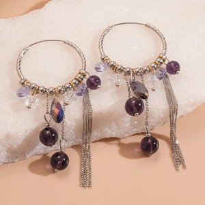 Detail of silver hoop earrings with purple beads and metallic chain tassels on stone