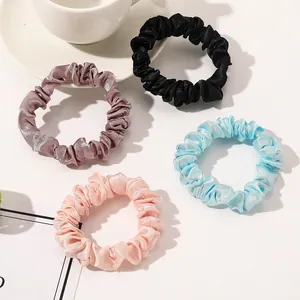 Close-up of four satin hair scrunchies in pastel colors on a bright minimalist background