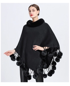 Detail of the black knit poncho featuring a plush faux fur collar and pom-pom tassels