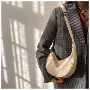 Detail of minimalist cream crescent bag with adjustable wide strap on a model