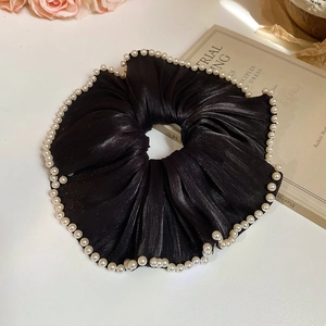 Detail of a black satin scrunchie with white pearl edges on a vintage background