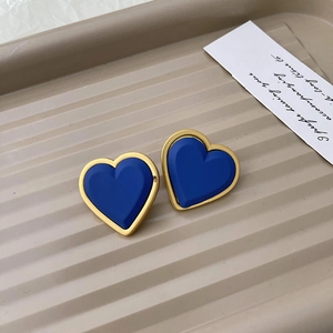 Macro shot of blue matte heart earrings with golden frame on a beige textured display tray