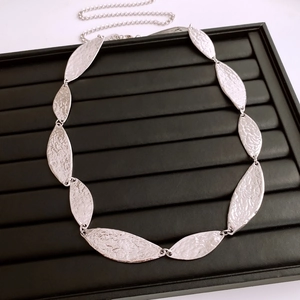 Close-up of silver leaf chain belt with textured hammered surface on black display