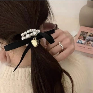 Detail of pearl hair tie with black velvet bow and gold heart pendant on low ponytail