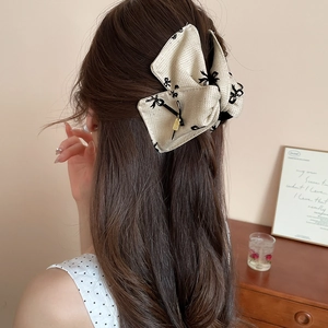 Beige acrylic bow hair claw clip with black floral print shown on a model hair bun